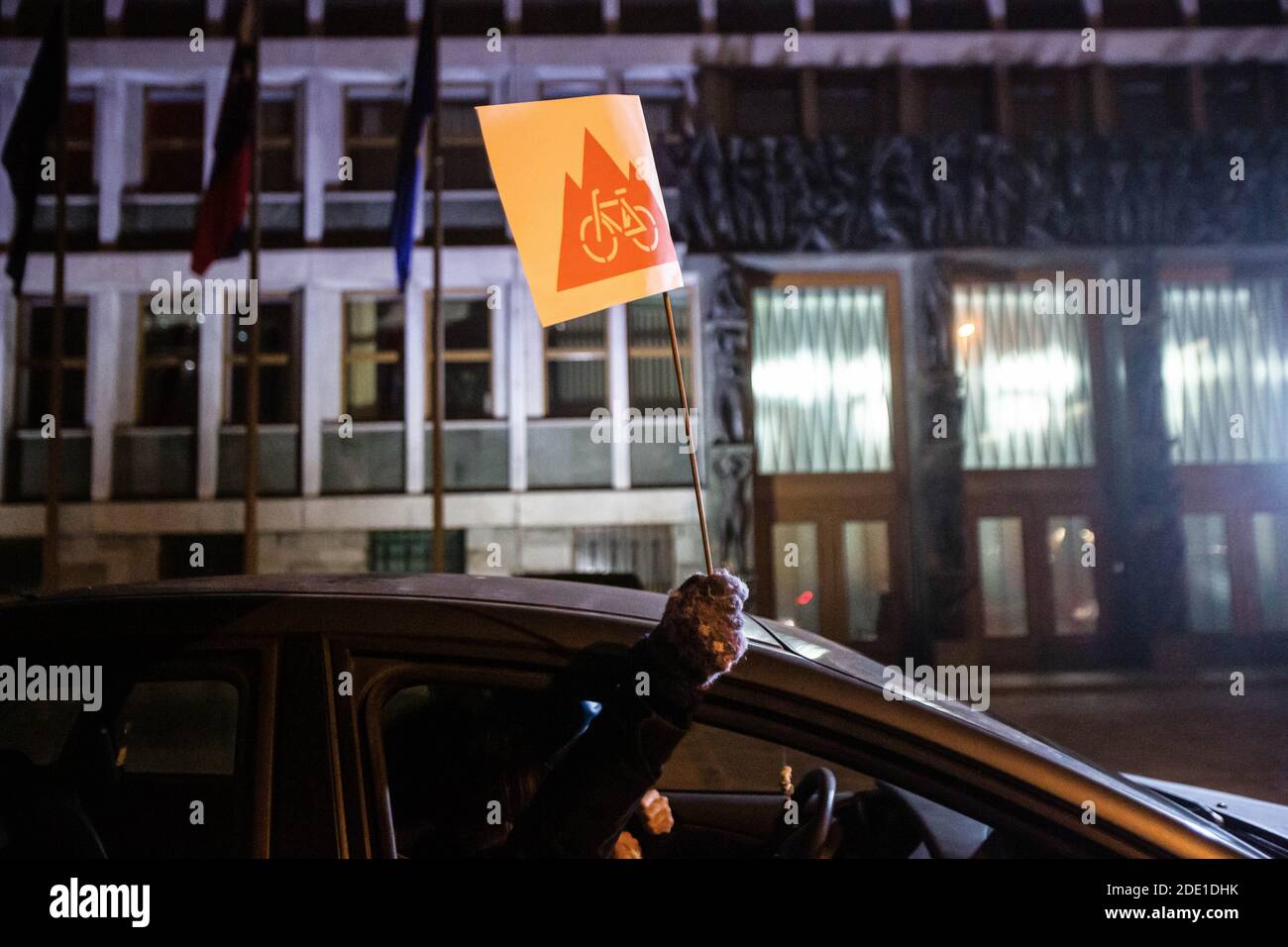 Un manifestante tiene in mano una bandiera contenente un simbolo di proteste anti-governative in Slovenia mentre si guida per l'edificio del parlamento durante una protesta anti-governativa.le proteste anti-governative nella capitale slovena sono proseguite con i manifestanti che in precedenza giravano per gli edifici governativi che ora guidavano nelle loro auto per rispettare l'epidemia di covid-19 restrizioni, in particolare il divieto del paese di raduni che sono soggetti a multe molto pesanti. Molti sono stati tuttavia prenotati e multati dalla polizia, che molti prendono come ancora un altro governo di spostare per criminalizzare le proteste. Foto Stock