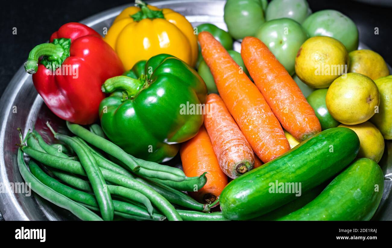 Fuoco selettivo di carote, peperone verde, fagioli verdi, cetrioli, limoni su un piatto con verdure assortite Foto Stock