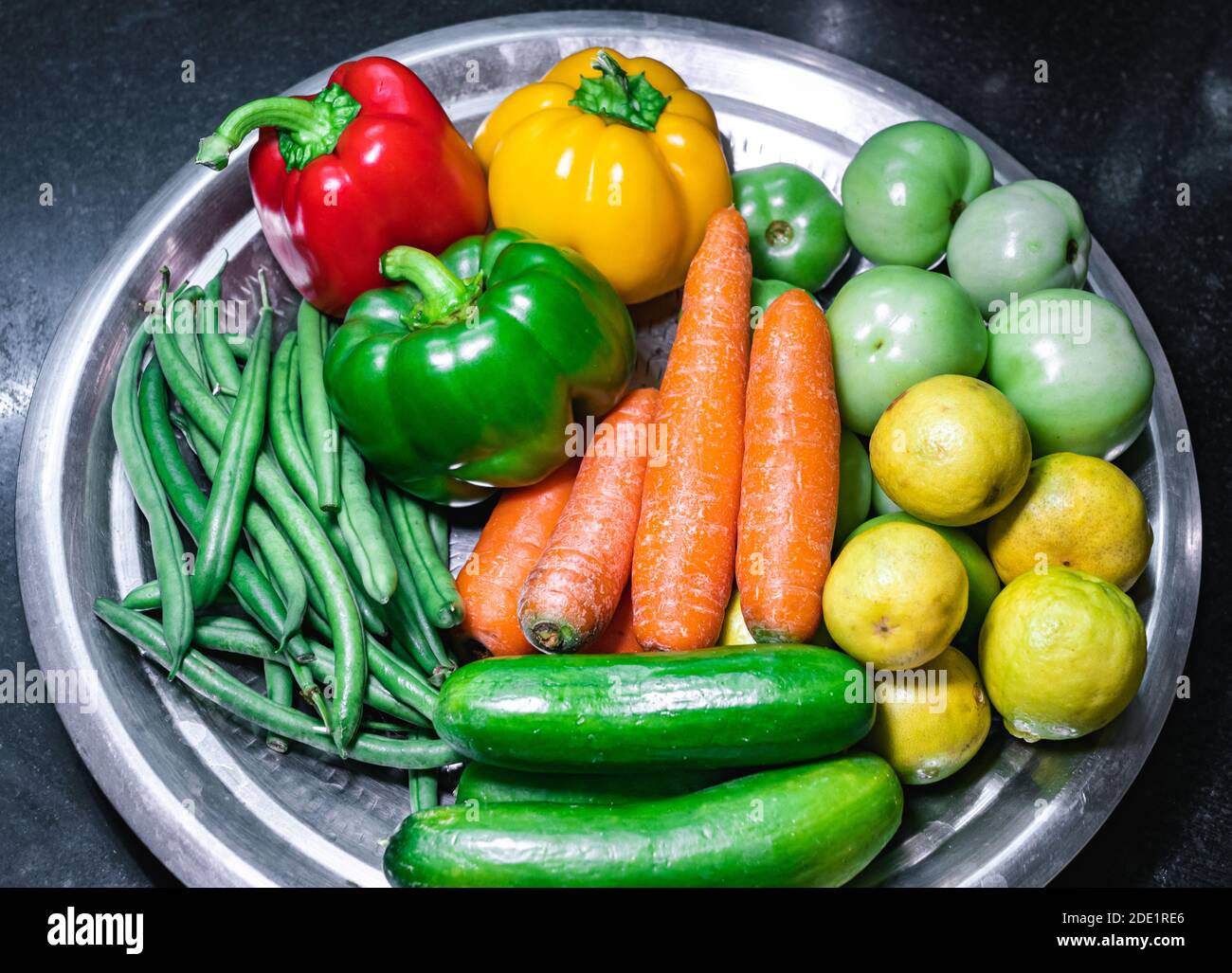 Verdure assortite di fagioli verdi, peperone rosso, peperone giallo, peperone verde, carote, cetrioli, pomodori verdi e limoni su un piatto Foto Stock