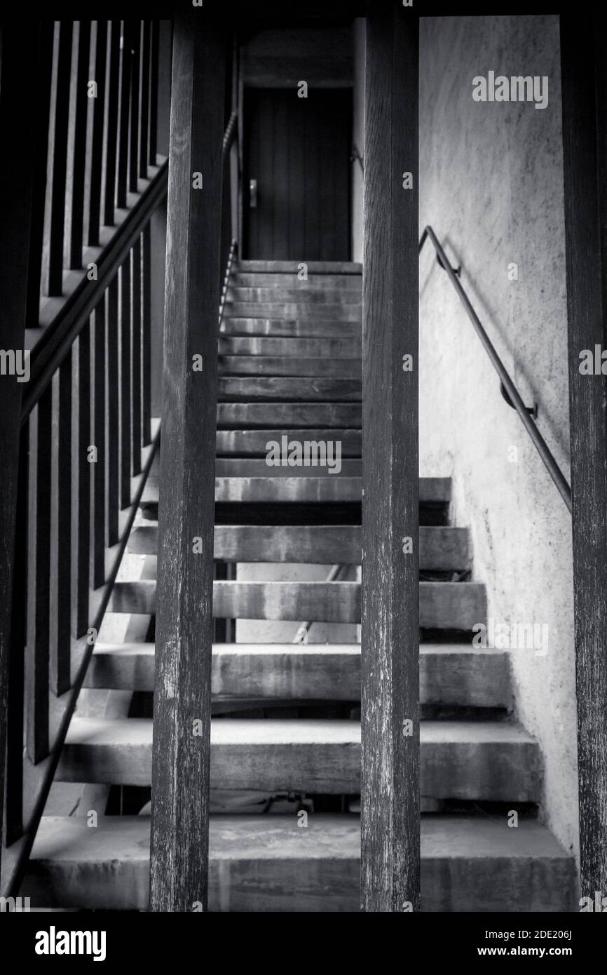 Primo piano immagine in bianco e nero di scale di legno che conducono verso l'alto verso una porta chiusa a chiave, vista attraverso un cancello barrato, Foto Stock