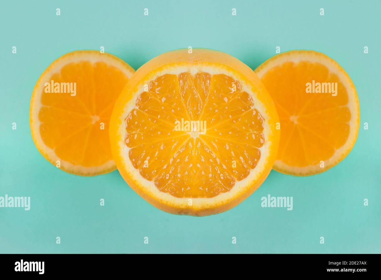 Polpa arancione brillante tagliata con due fette sui lati, formando un'elegante composizione geometrica su uno sfondo di carta blu. Cucina creativa. Foto Stock