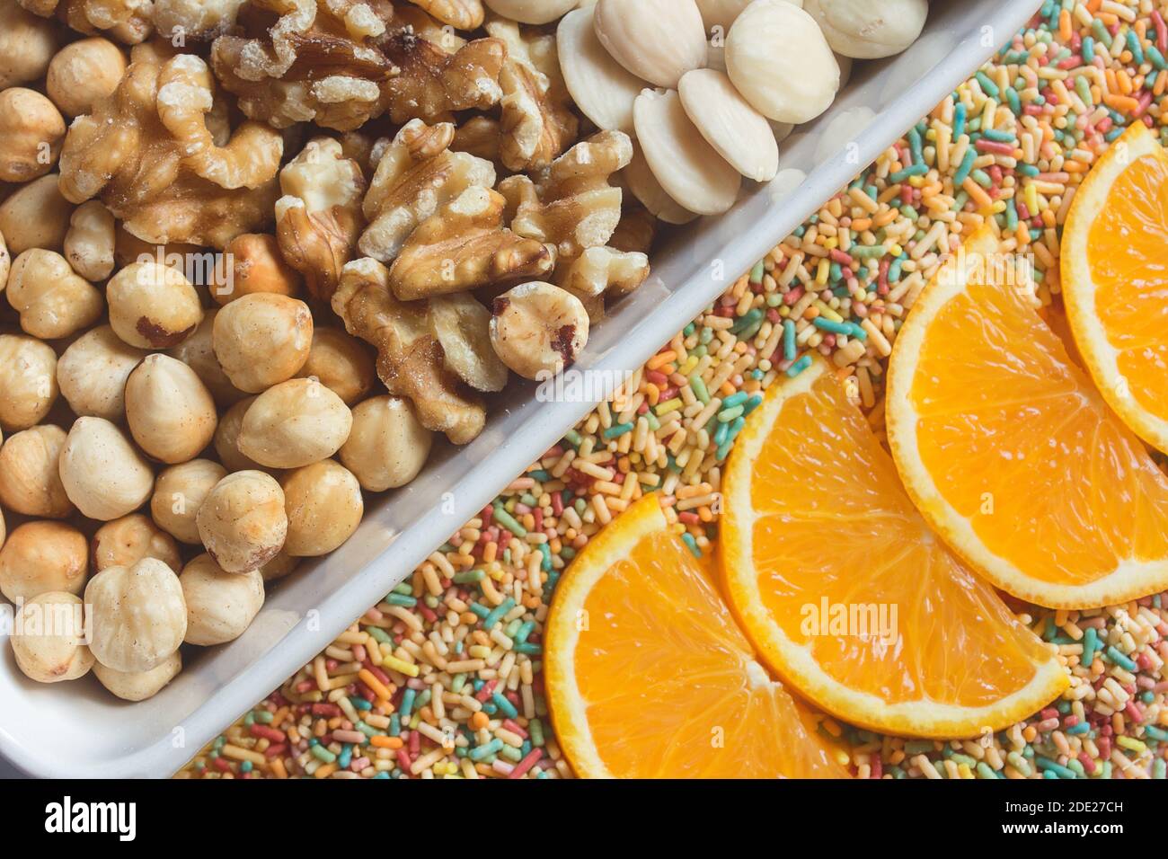 Un assortimento di frutta secca mista, noci, mandorle e nocciole con fette di arancia su spaghetti di zucchero colorati. Dessert di cucina creativi Foto Stock