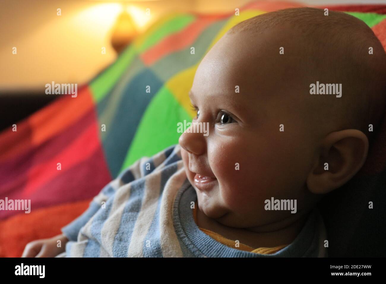 Bambino di tre mesi sulla coperta colorata guardando la macchina fotografica. Vista laterale Foto Stock