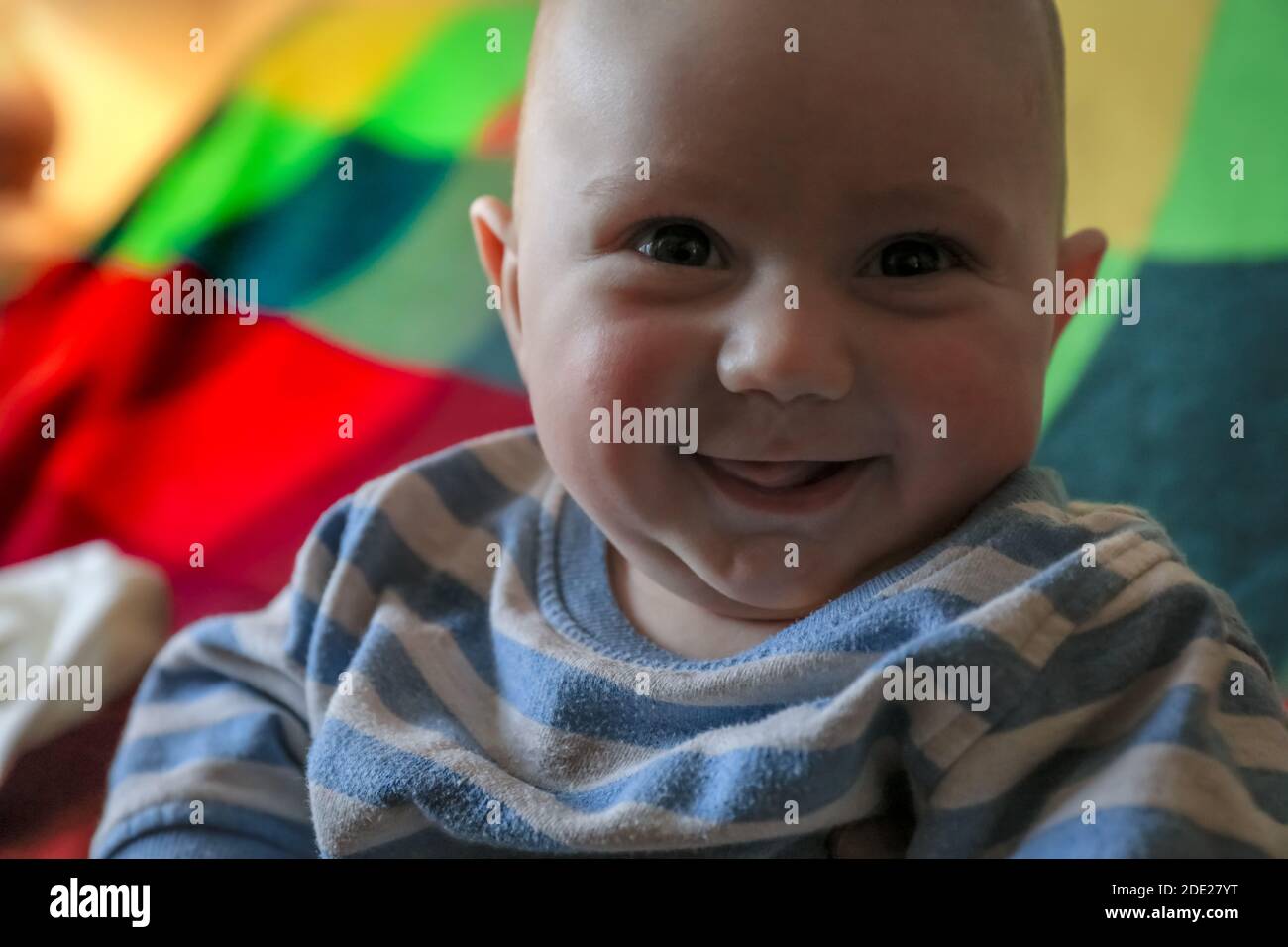 Bambino di tre mesi sulla coperta colorata guardando la macchina fotografica. Vista frontale Foto Stock
