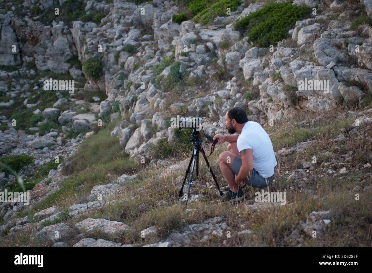 Fotografo che scatta foto al tramonto sulla costa rocciosa Foto Stock