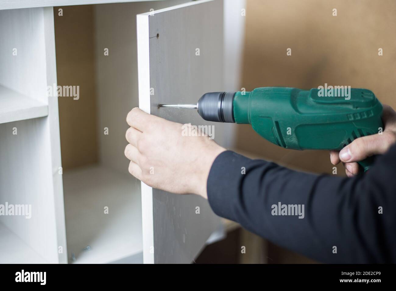Il padrone tiene un pugliatore nelle mani e fora un buco. Concetto di noleggio di utensili elettrici. Produzione di mobili Foto Stock