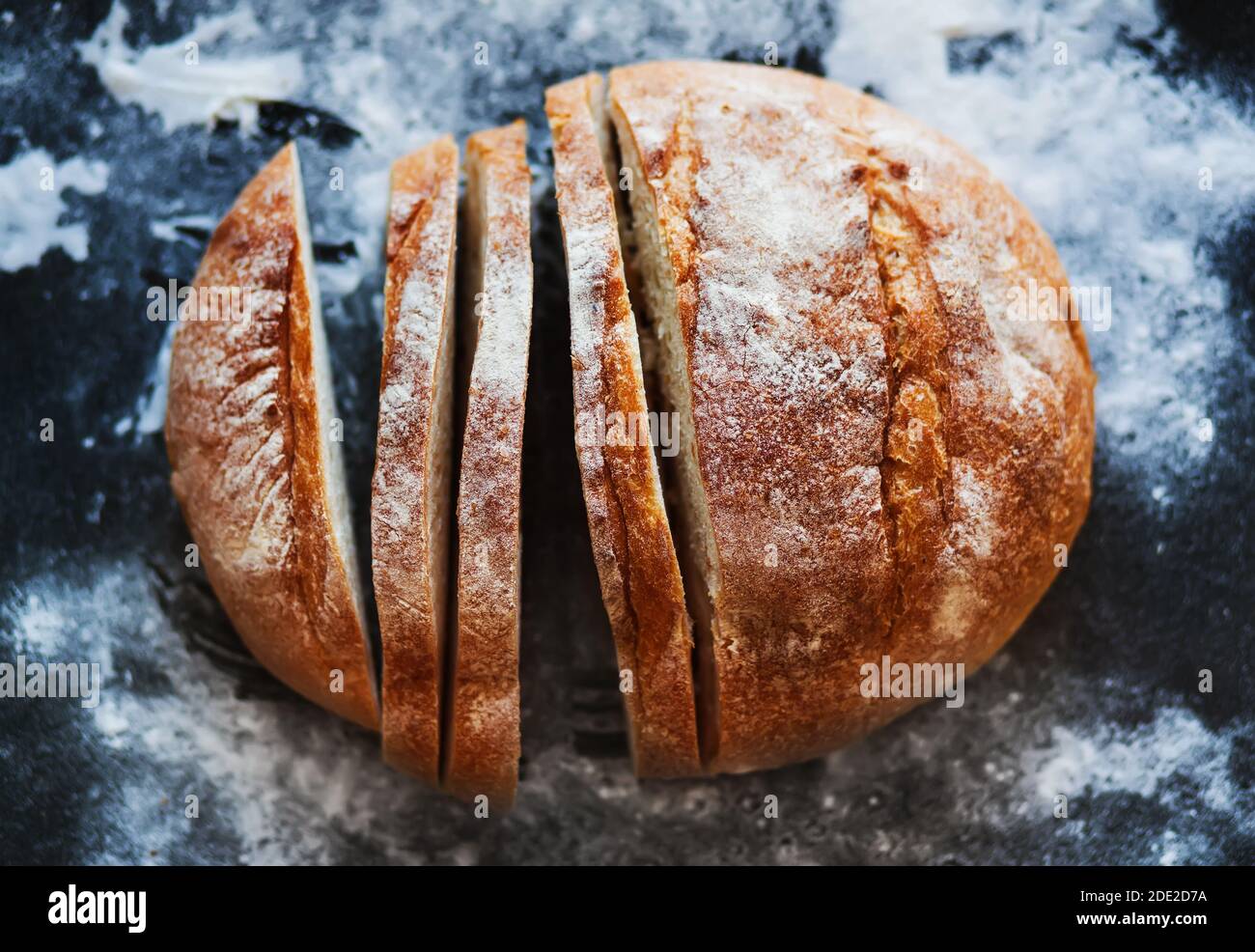 Vista dall'alto del pane di grano a fette appena cotto e leggermente infarinato. Prodotti da forno. Cucina casalinga. Foto Stock