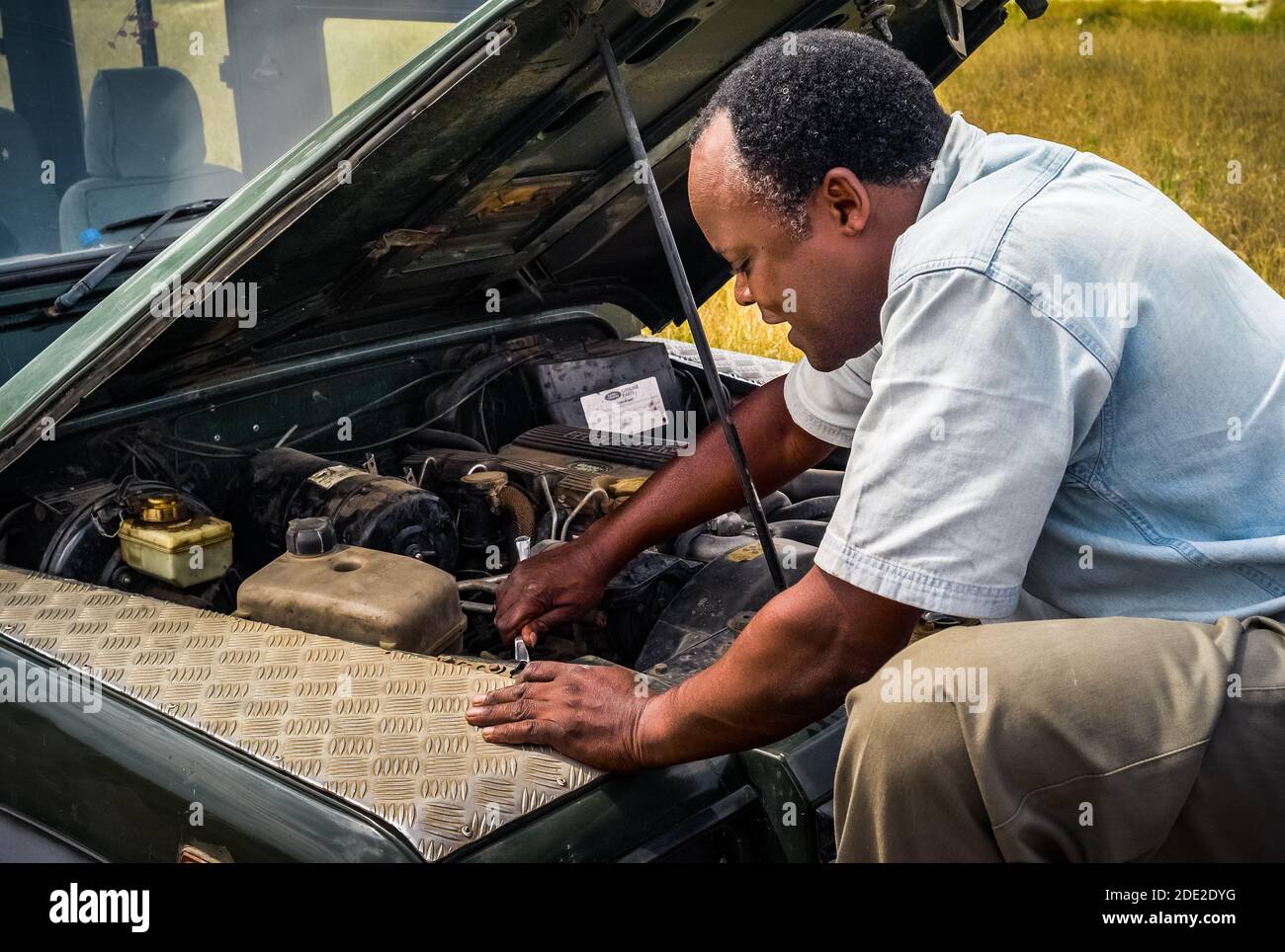Serengeti, Tanzania - 3 luglio 2008: Uomo nero che ripara una jeep Landrover Safari in Africa. Un conducente africano che ripara un veicolo 4x4 dopo un guasto. Foto Stock