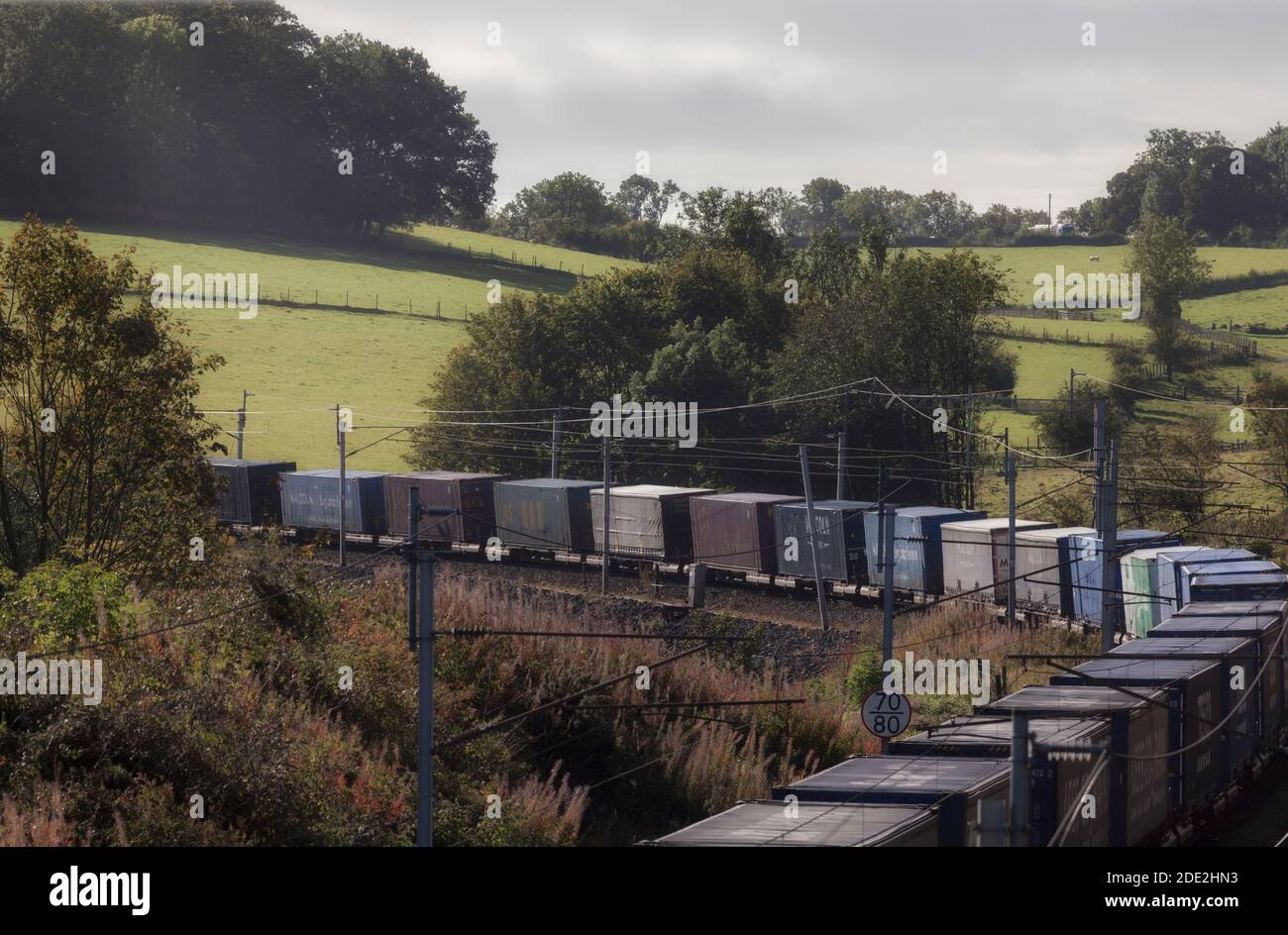 Container su un treno merci che si dirige intorno ad un angolo La linea principale della costa occidentale di Cumbria Foto Stock