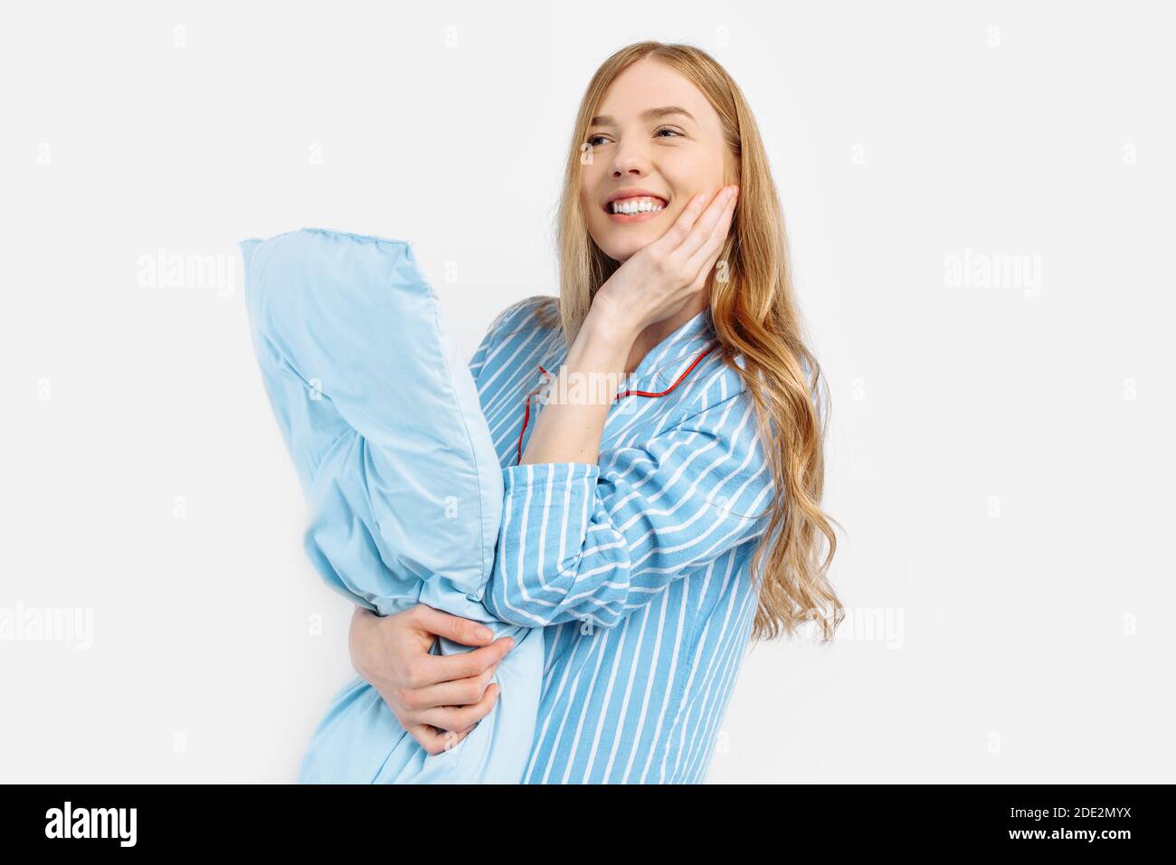 Ritratto di bella ragazza pensiva in pigiama tenendo cuscino, sognatore prima di andare a letto per vedere dolci sogni, su sfondo bianco Foto Stock