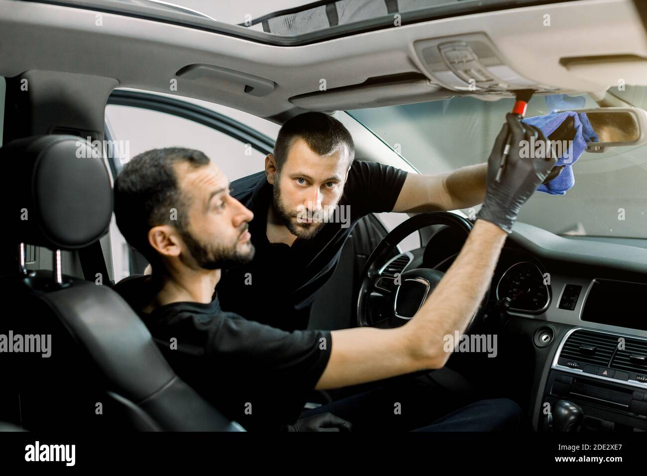 Due bei lavoratori di servizio auto maschile pulizia interni auto moderna.  Concentrarsi sull'uomo, pulire lo specchio dell'auto con un panno in  microfibra, mentre il suo collega Foto stock - Alamy