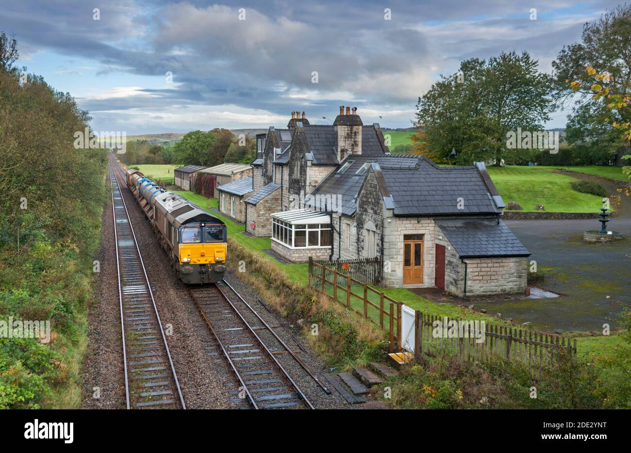 Direct Rail Services classe 66 trasporto locomotiva rete ferroviaria Treno di trattamento che si occupa di foglie autunnali passando l'Arkholme chiuso stazione Foto Stock