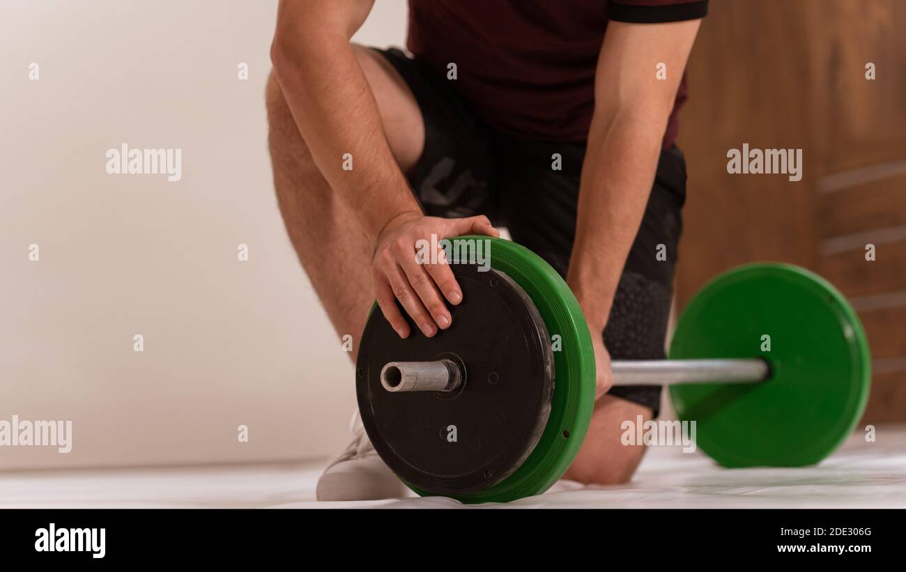 Giovane uomo si inchino su un ginocchio preparando accessori per il fitness tono nero e verde, attrezzature per il concetto di allenamento del peso. Attrezzature sportive maschili per l'allenamento Foto Stock