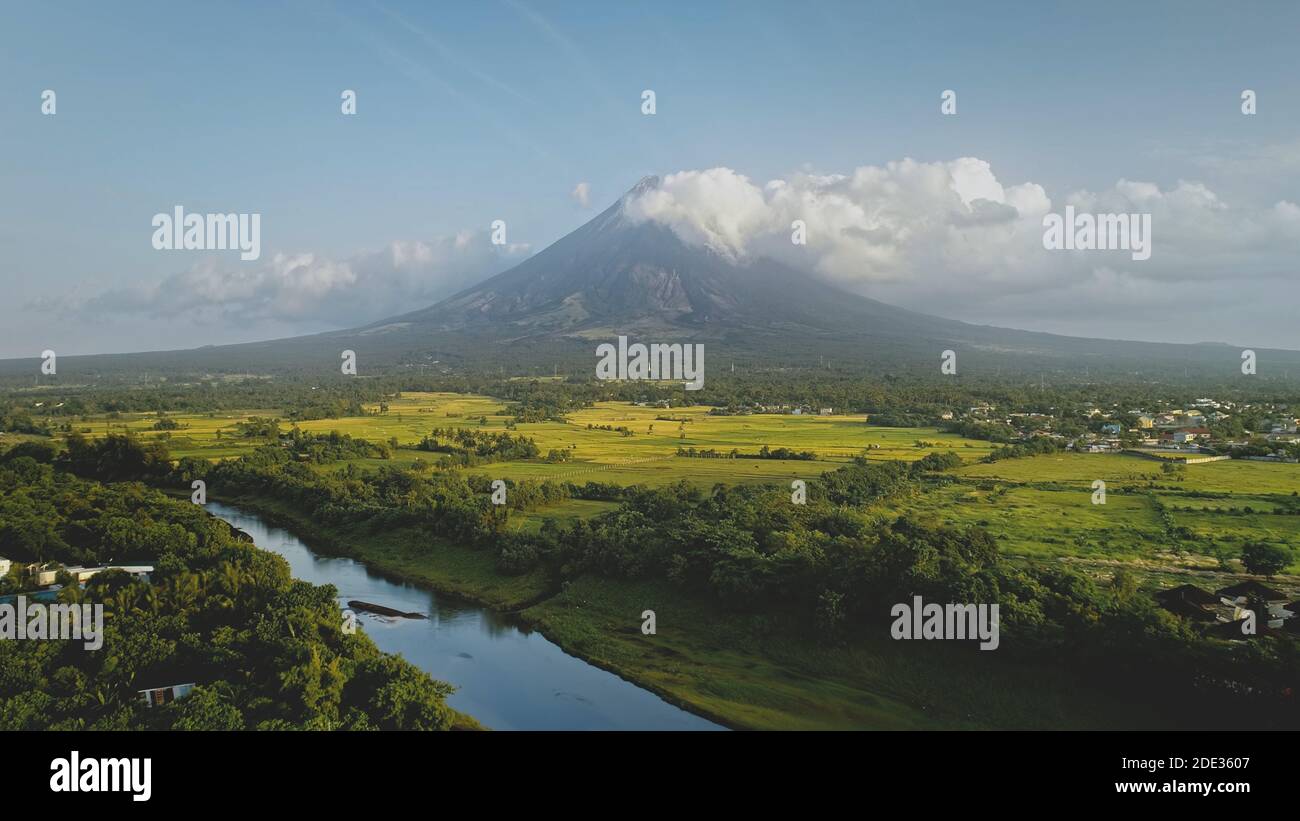 Hillside fiume a eruzione vulcano con erba verde riva a Filippine Campagna aerea. Campi, valle, prati di nessuno paesaggio naturale. Scenografica cinematografica del monte Mayon erutta alla foschia Foto Stock