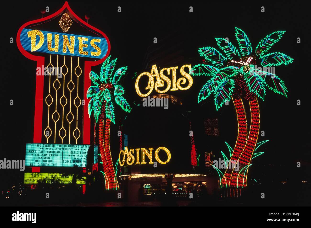 Al neon e ad altre luci colorate, queste insegne all'aperto per il Dunes Hotel e il suo Casinò Oasis si distinguono di notte lungo Las Vegas Boulevard, meglio conosciuto come Strip, una strada fiancheggiata da spettacolari hotel e casinò a sud dei confini della città di Las Vegas, Nevada, USA. Le dune aprirono nel 1955, una delle prime attrazioni di questa famigerata destinazione desertica, famosa per il suo gioco d'azzardo e i suoi bei tempi. Quando l'hotel fu demolito nel 1993 per fare spazio al nuovo mega resort Bellagio, questi segni distintivi e palme al neon furono perduti nella storia. Foto Stock