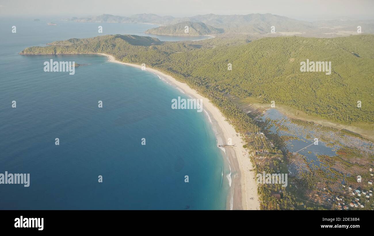 Mare tropicale sole di mare baia aerea. Spiaggia di sabbia con alberi tropicali verdi in campagna Filippine. Case e logge nella foresta verde sulla costa dell'oceano. Montagne colline a nessuno paesaggio naturale Foto Stock