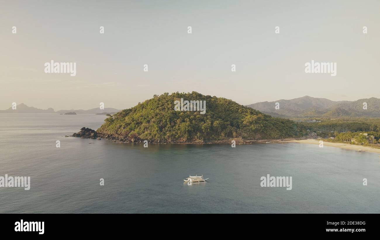 Montagne verdi a baia di mare con barche aeree. Tropic resort presso la spiaggia di sabbia. Palme verdi sulla costa dell'oceano. Le persone riposano alle navi passeggeri. Crociera estiva alle Filippine, Isola di El Nido Foto Stock