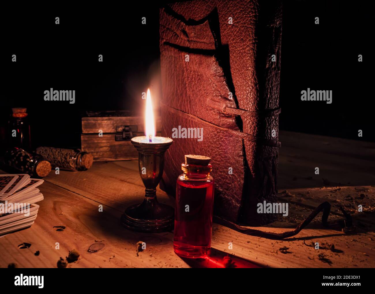 Immagine di un tomo legato in pelle, bottiglie di vetro con liquido ed erbe, una candela e tarocchi carte su un tavolo di legno Foto Stock