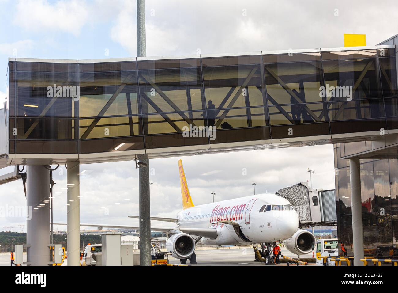 I passeggeri camminano attraverso il ponte di imbarco passeggeri nel terminal dell'aeroporto. Un aereo sullo sfondo. Aeroporto Sabiha Gokcen. Foto Stock