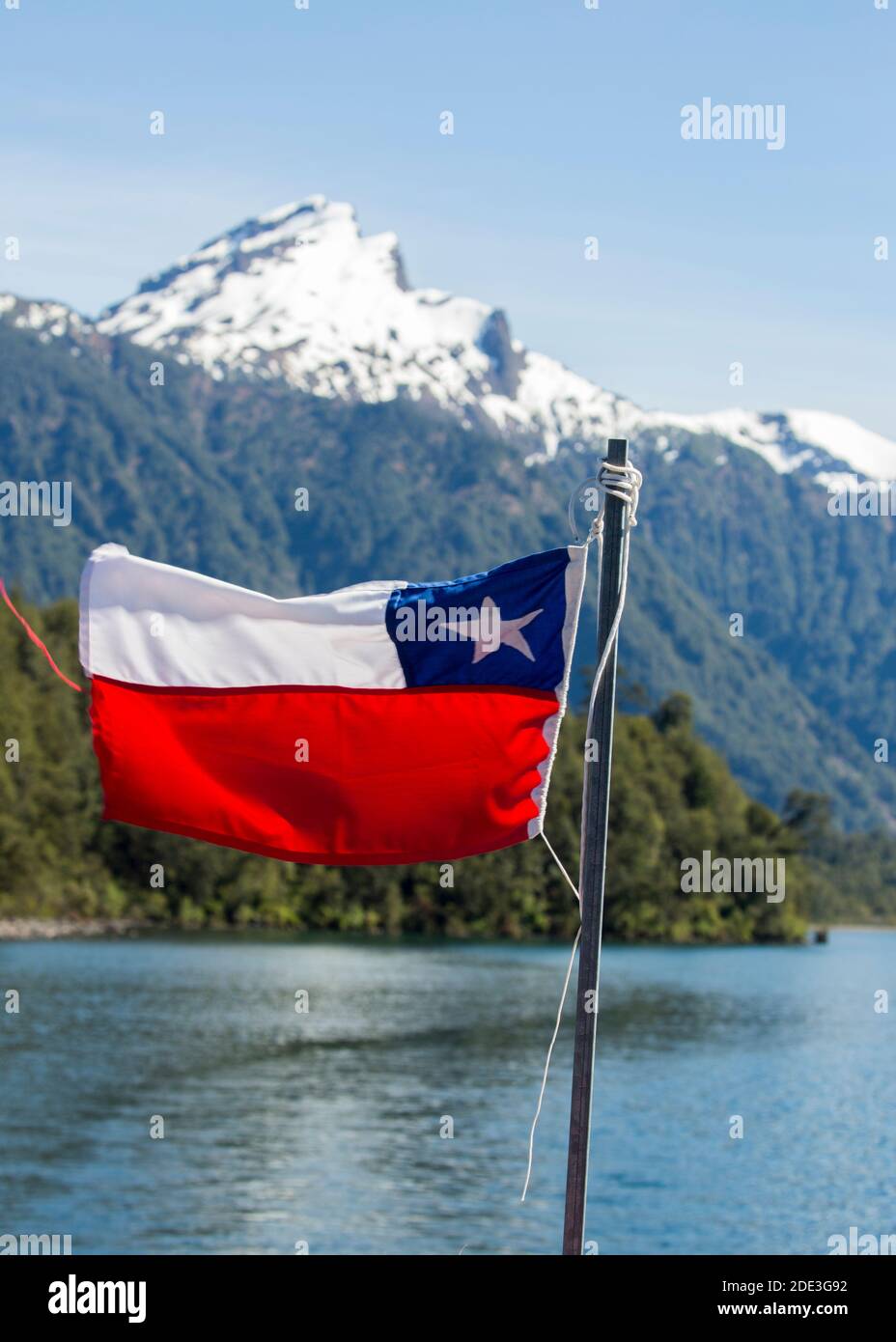 La bandiera cilena che vola su un traghetto tra Cile e Argentina sul Lago Todos Los Santos, Petrohue, Cile, con vulcano innevato in lontananza Foto Stock