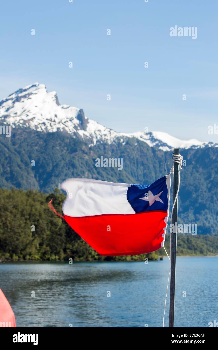 La bandiera cilena che vola su un traghetto tra Cile e Argentina sul Lago Todos Los Santos, Petrohue, Cile, con vulcano innevato in lontananza Foto Stock
