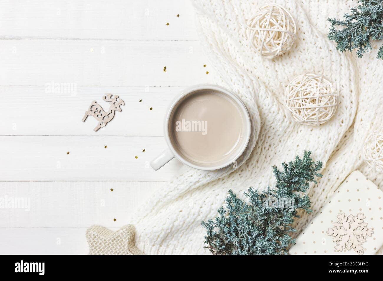 Accoglienti momenti mattutini a casa con una tazza di caffè, una coperta calda, un albero sempreverde e ornamenti su sfondo di legno bianco. Inverno, concetto di vacanza. Piatto Foto Stock