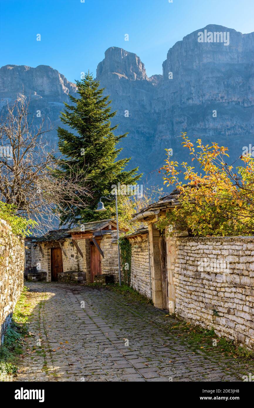 Architettura tradizionale con una stretta strada in pietra e la montagna astraka AS Contesto durante la stagione autunnale nel villaggio di Papigo a zagori Grecia Foto Stock