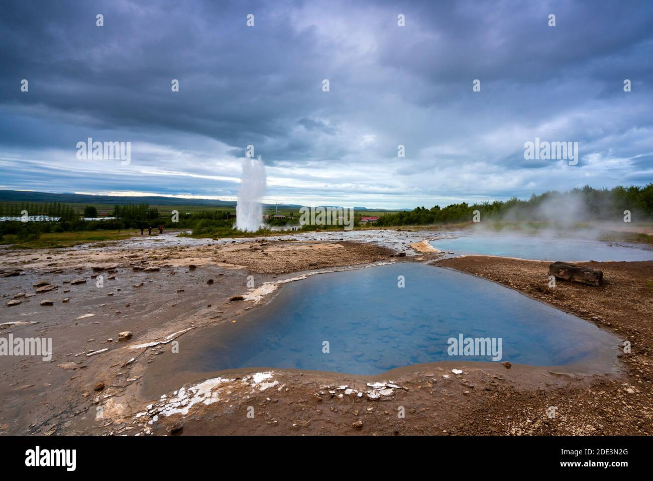 Vista panoramica del laghetto blu sulla zona geotermica con il geyser Strokkur che erutta sullo sfondo, Geysir, Islanda Foto Stock