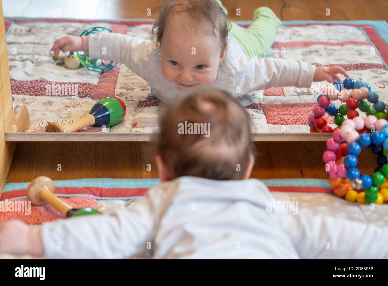 Una bambina di 4 mesi sdraiata sulla pancia e facendo un 'volo aereo' o estensione spinale completa, sollevando entrambe le braccia e le gambe dal pavimento Foto Stock