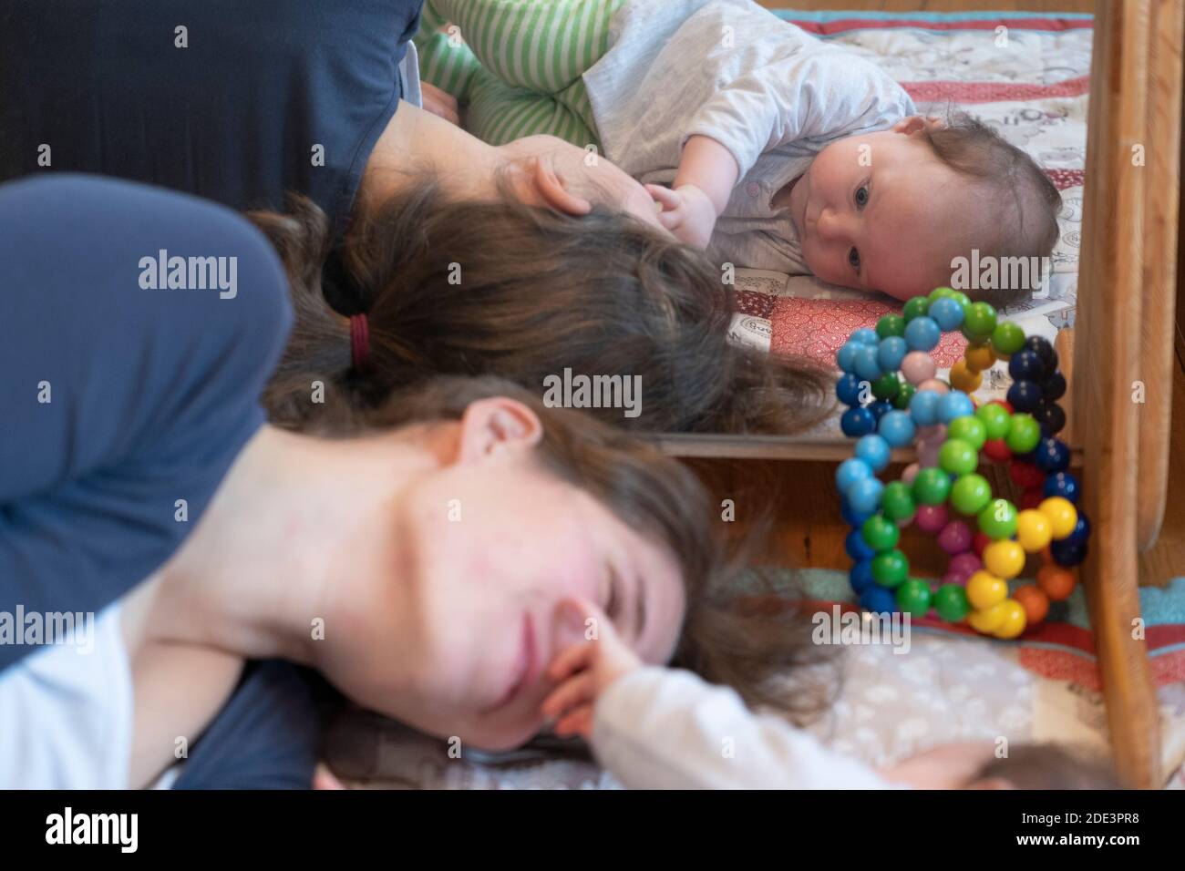 Una madre che interagisce e gioca con la sua bambina di 4 mesi, con entrambe sdraiate su un tappeto da gioco con uno specchio dietro, Regno Unito Foto Stock
