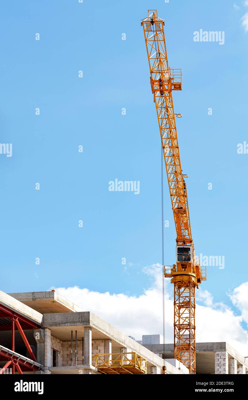 Un braccio di gru a torre salta sopra un cantiere contro un cielo blu chiaro, immagine verticale, spazio di copia. Foto Stock