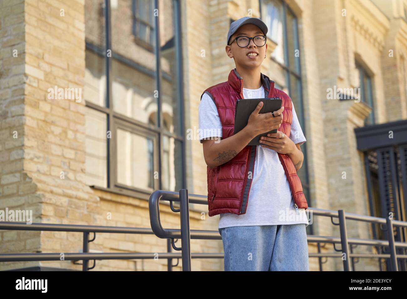Ordine di monitoraggio. Corriere maschile asiatico giovane utilizzando app su tablet digitale mentre si è in piedi per strada. Concetto di servizi di consegna Foto Stock