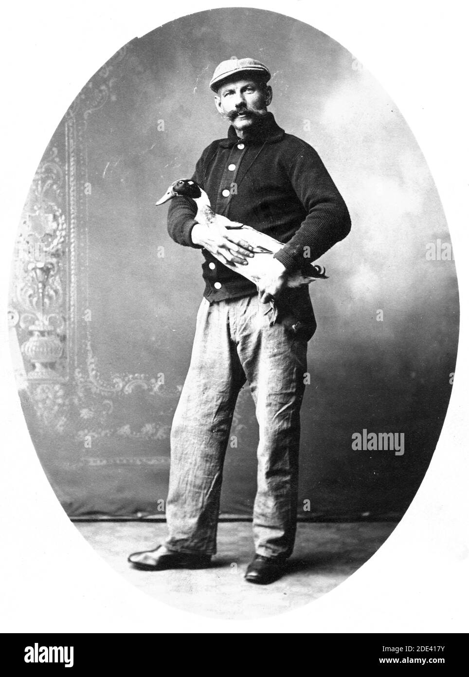 Nel 1913, questo uomo amava tanto il suo animale domestico, o era così orgoglioso del suo ottimo prodotto agricolo, che portava questa grande anatra allo studio di fotografia locale per fare la loro fotografia per la sua famiglia e gli amici. L'anatra sembra soddisfare con tutto; probabilmente non vede il suo proprio futuro. Il Signore ha un baffi fine, e indossa un comodo cappuccio, un caldo maglione a bottoni con colletto, e pantaloni rugosi. Per vedere le mie altre immagini insolite, cerca: Pristor vintage dispari Foto Stock