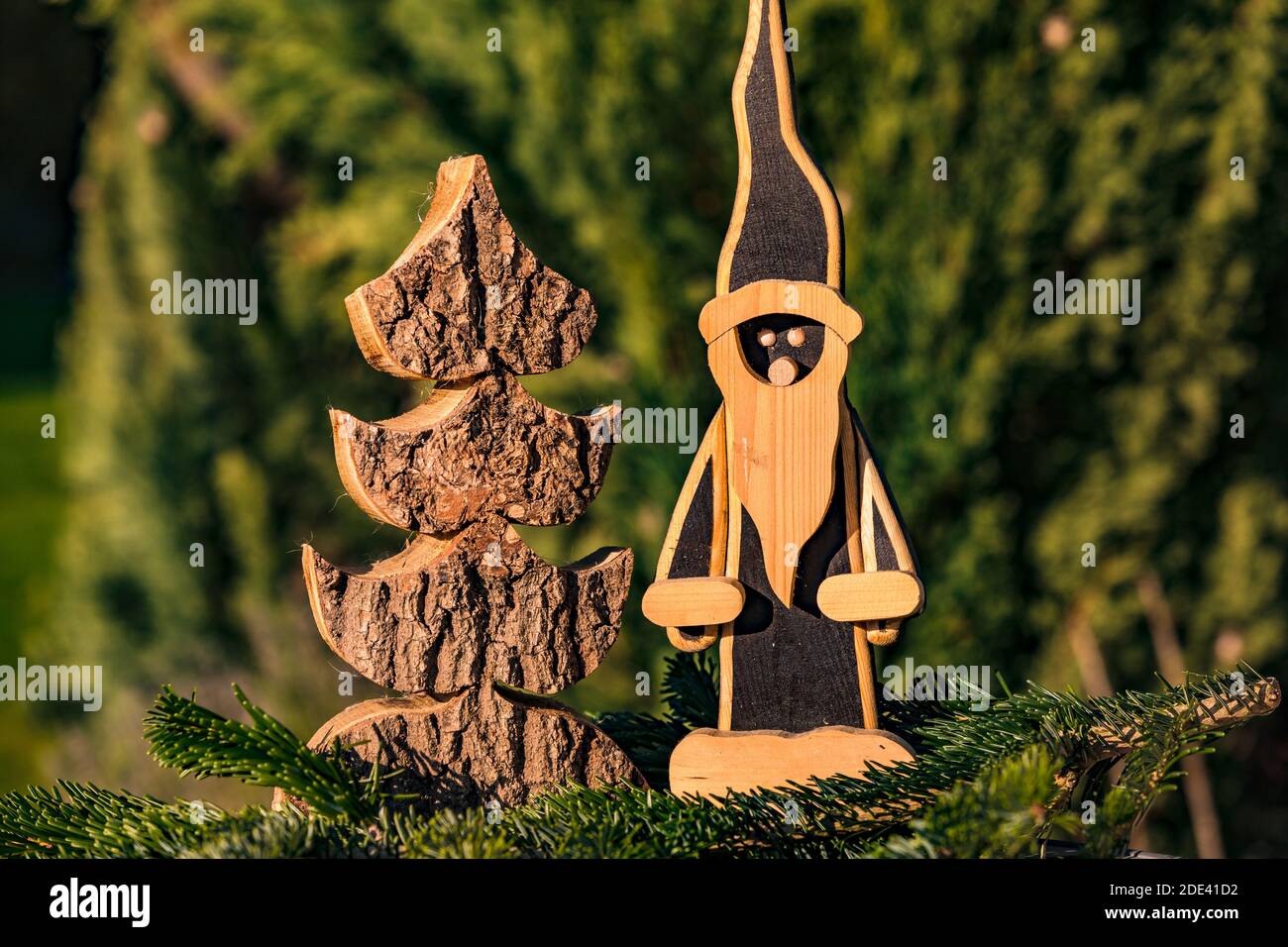 Un classico Babbo Natale in legno accanto a un albero di Natale in legno, splendidamente tagliato di fronte a una verde foresta di conifere Foto Stock