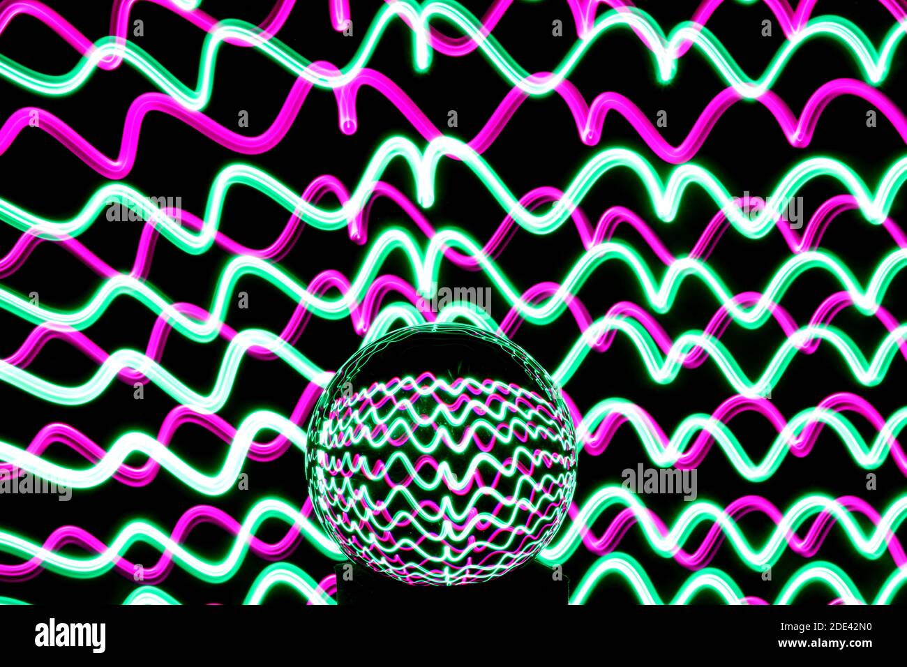 Fotografia a lunga esposizione di neon multicolore in un modello astratto di turbolenza con sfera di vetro riflettente. Fotografia di pittura leggera. Foto Stock