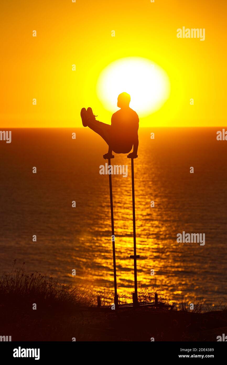 Un ginnasta esegue un v-sit mentre si silhouette contro il tramonto a Black's Beach, San Diego, CA. Foto Stock
