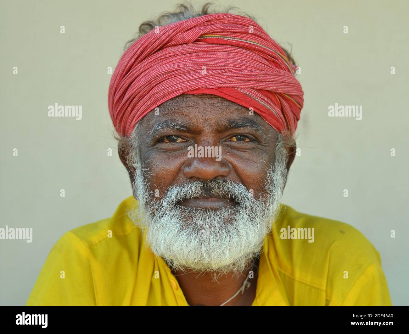 Positivo anziano amichevole indù indiano pellegrino con turbano rosso e la camicia gialla pone per la macchina fotografica. Foto Stock