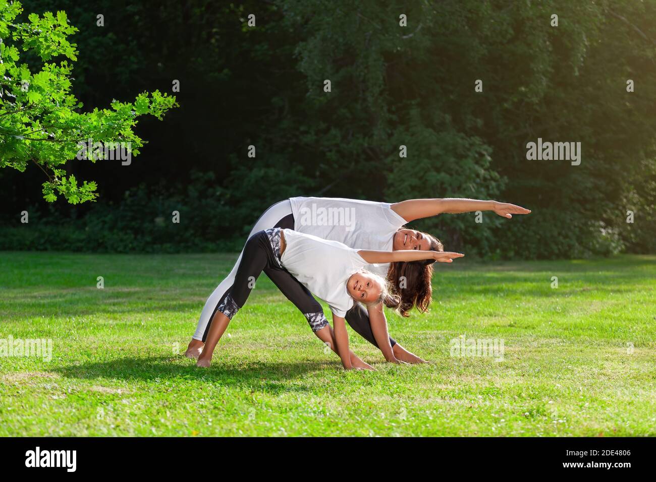 Madre e bambina insieme sta facendo yoga asana o pilates allenamento su erba verde nel parco estivo e sorridente. Concetto di famiglia outd Foto Stock