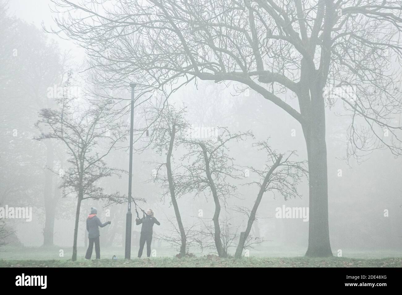 Stretching con bande reistance e un personal trainer, mantenersi in forma in una giornata di nebbia in un parco londinese in inverno Foto Stock