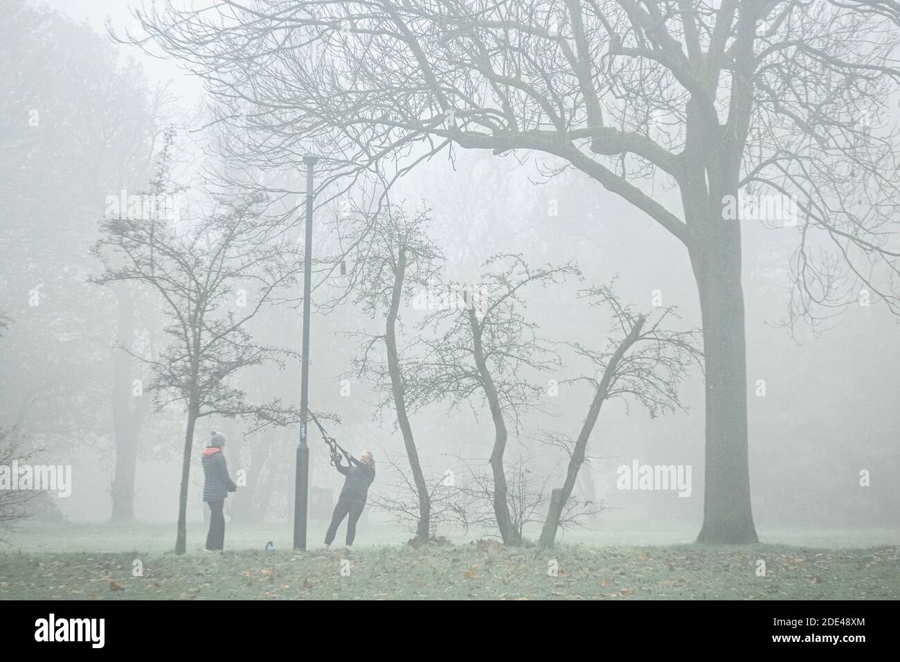 Stretching con bande reistance e un personal trainer, mantenersi in forma in una giornata di nebbia in un parco londinese in inverno Foto Stock