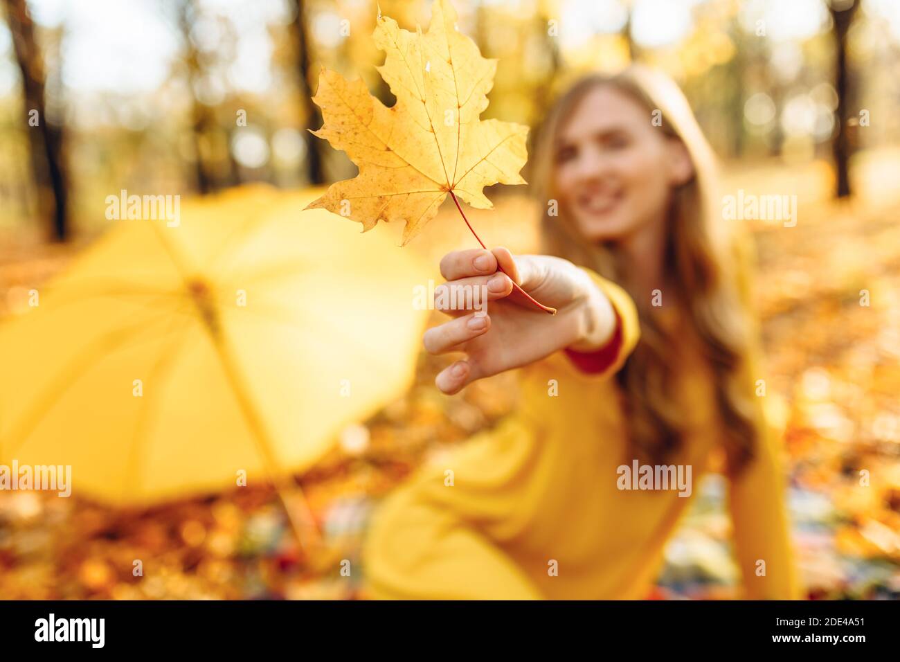 Bella giovane ragazza sorridente in autunno Parco seduta su coperta Tenendo le foglie d'autunno in mano godendo il caldo clima soleggiato Foto Stock