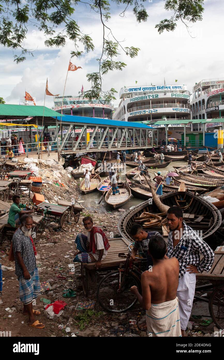 Quattro uomini in conversazione, porto, dietro di esso traghetti fluviali e piccole barche, Dhaka, Bangladesh Foto Stock