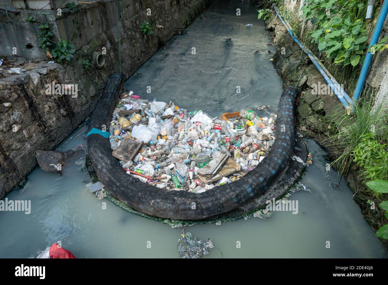 Una barriera realizzata in bottiglie di plastica riciclata racchiuse in rete teso lungo un canale d'acqua cattura una grande quantità di plastica bottiglie che altro Foto Stock