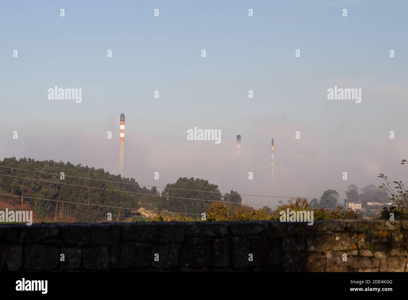 Torri di evacuazione dei gas della raffineria la Coruña nel nebbia al tramonto Foto Stock