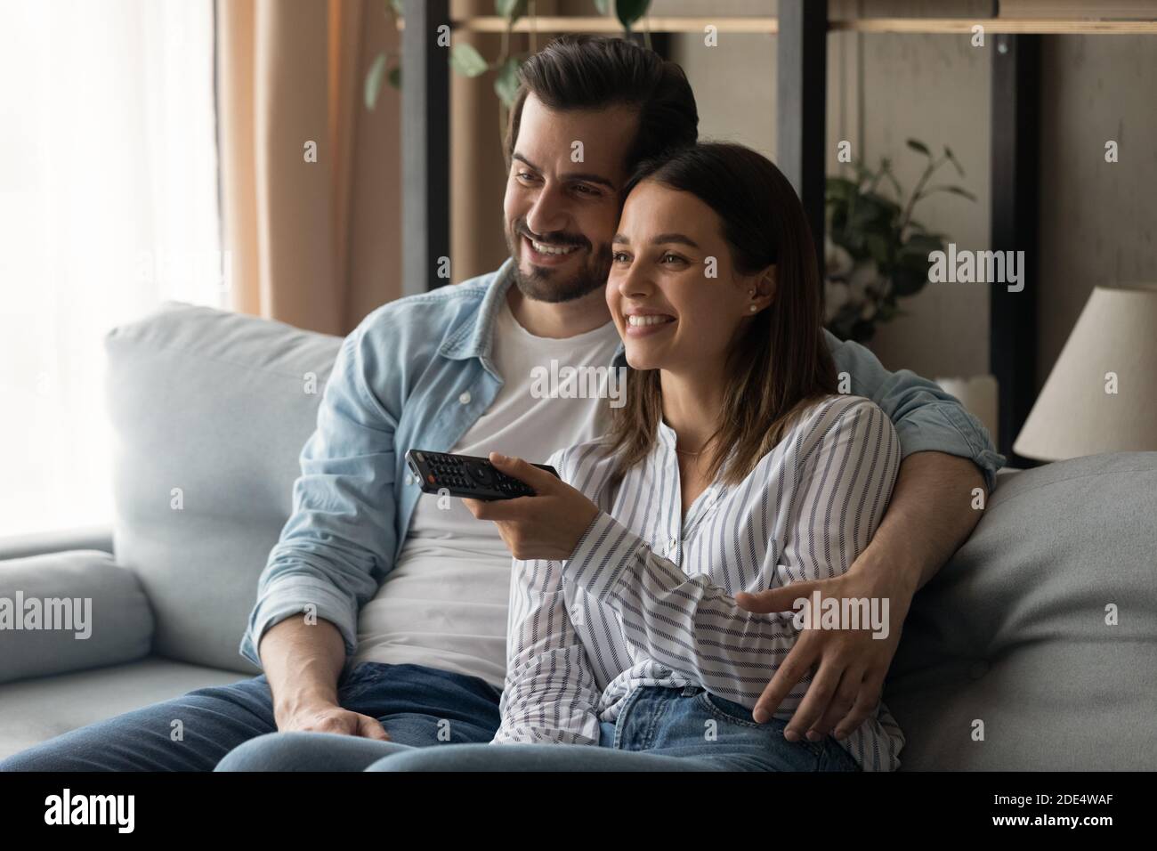 Una giovane coppia sorridente si rilassa sul divano guardando la TV Foto Stock