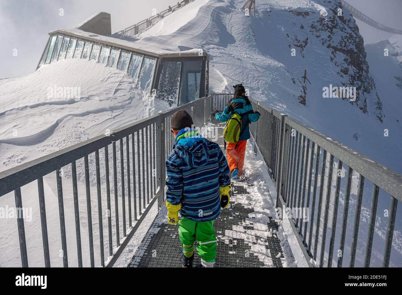 Vista posteriore di due bambini che camminano sul ponte sulla cima della montagna. Vacanze invernali con bambini nelle Alpi. Glacier 3000, les Diablerets Foto Stock