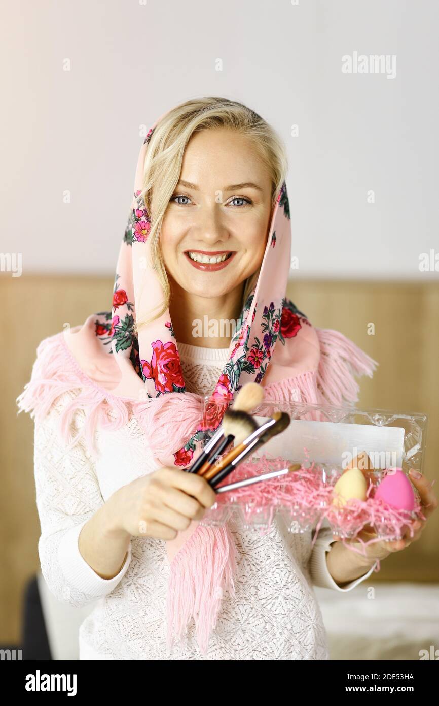 Donna caucasica sorridente che tiene un cestino con le uova di Pasqua colorate in camera soleggiata Foto Stock