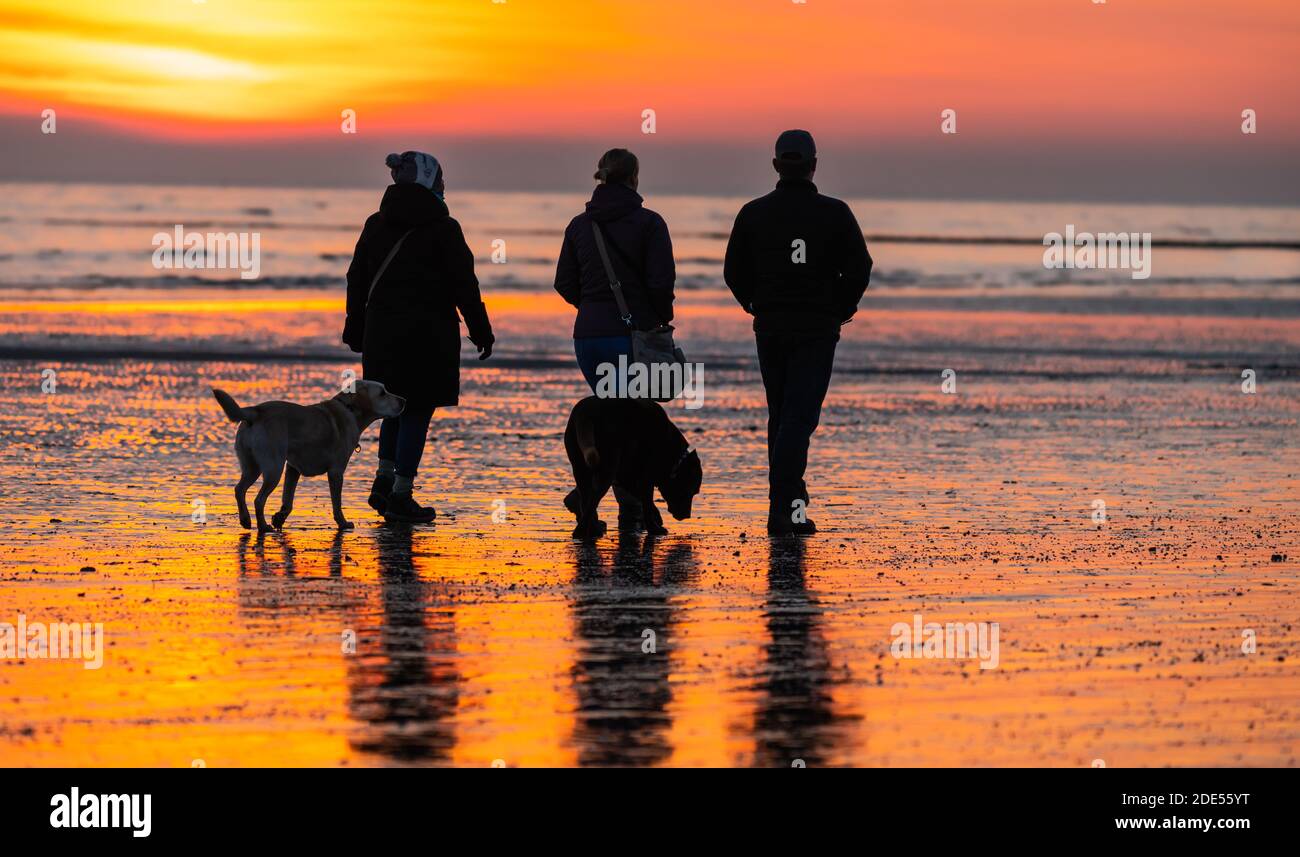 3 persone prendono un paio di cani per una passeggiata lungo la spiaggia con la marea fuori al tramonto serale a Littlehampton, West Sussex, Inghilterra, Regno Unito. Foto Stock