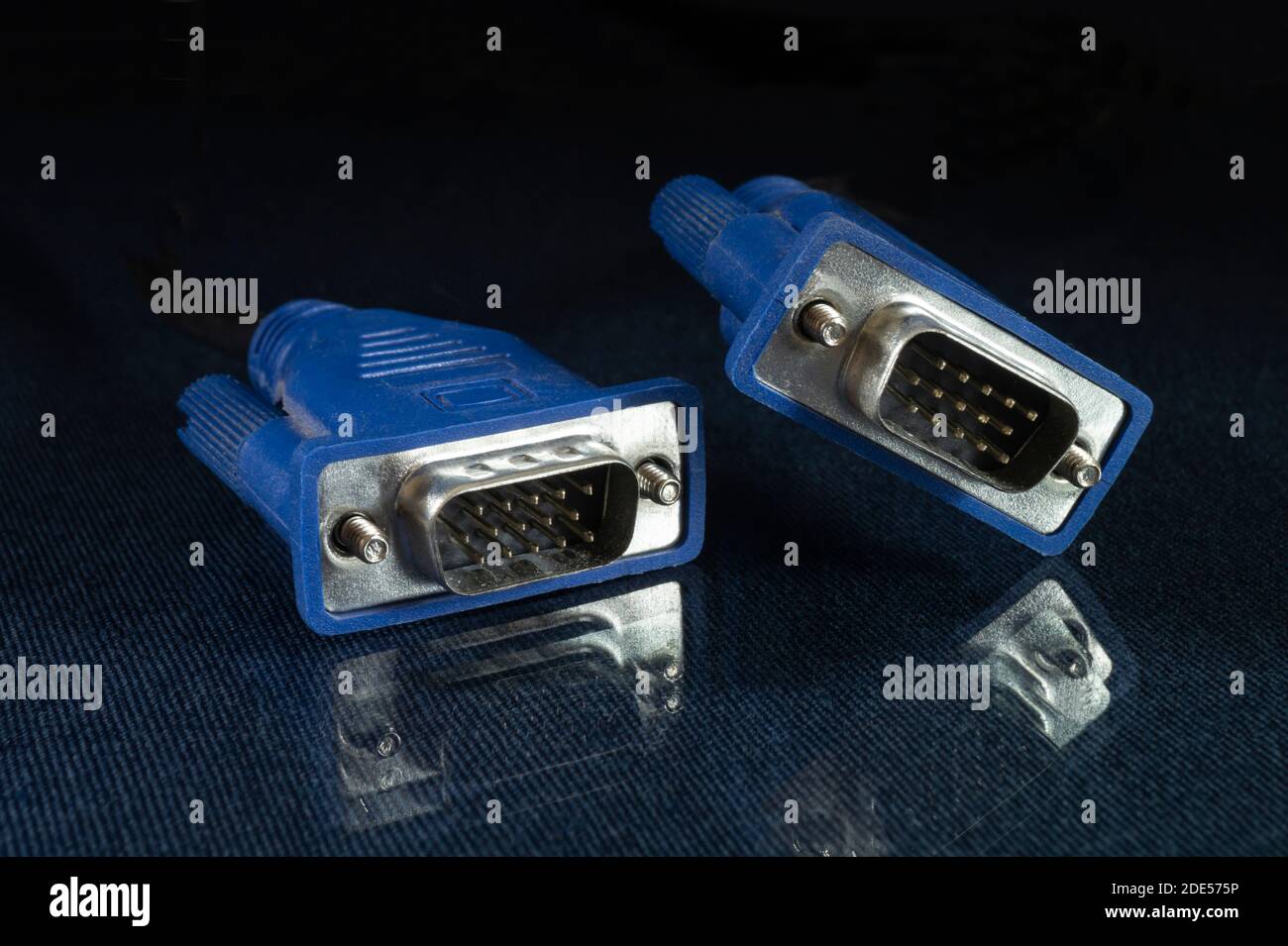 Il cavo per il collegamento del monitor poggia su un tavolo di vetro con riflessione. Connettore blu su sfondo nero Foto Stock