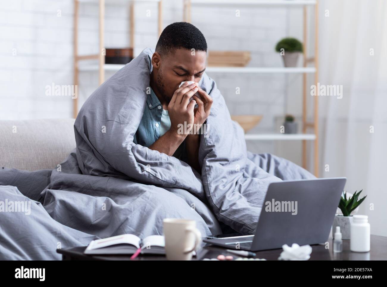 L'uomo africano malato starnutisce e soffia il naso seduto a casa Foto Stock